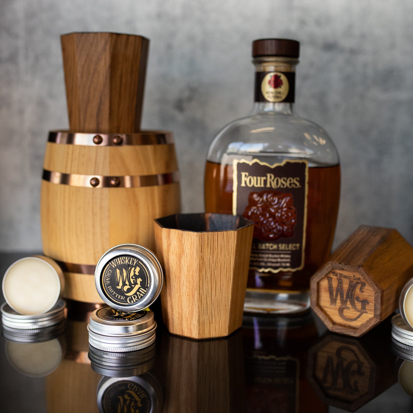 A tin of Grail butter displayed next to Four Roses Whiskey and a Whiskey Grail.